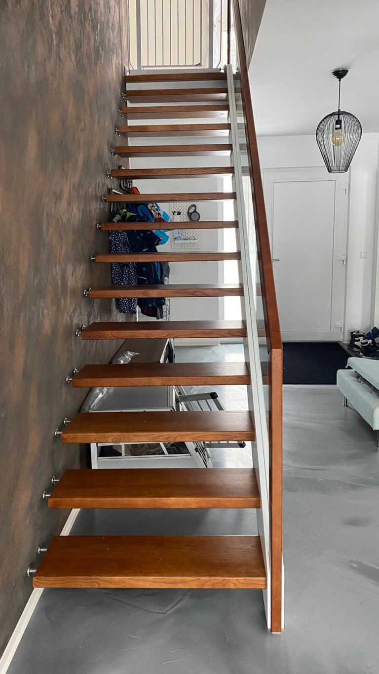 W-34 Holzwangentreppe, gerade, Stufen aus Esche gebeizt, Glasgeländer, Klarglas, Wangen in Weiß, Gummibolzen, Brett für Mauer